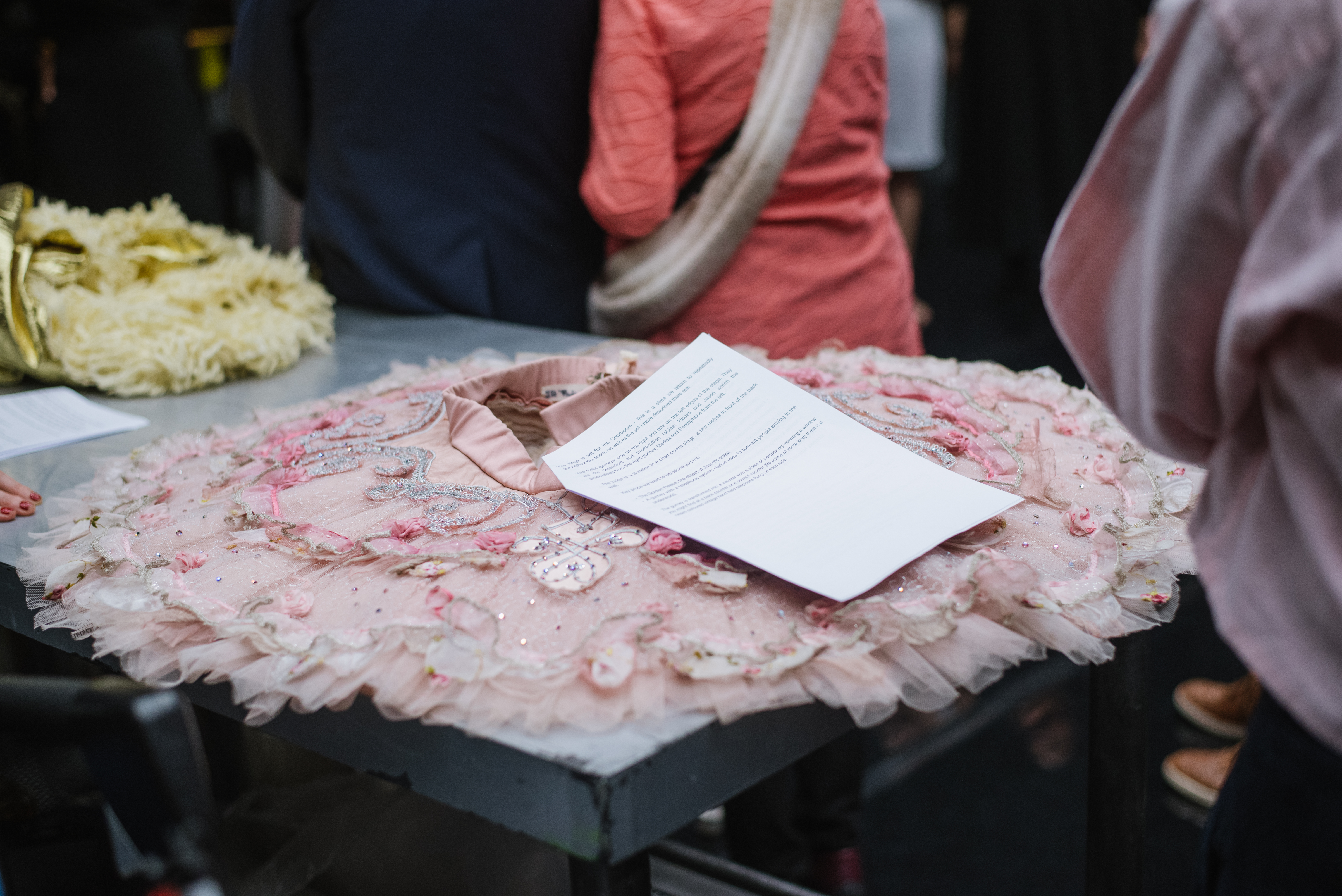 A sparkly pink tutu lies flat on a black table. A woman in a pink shirt stands behind the table.