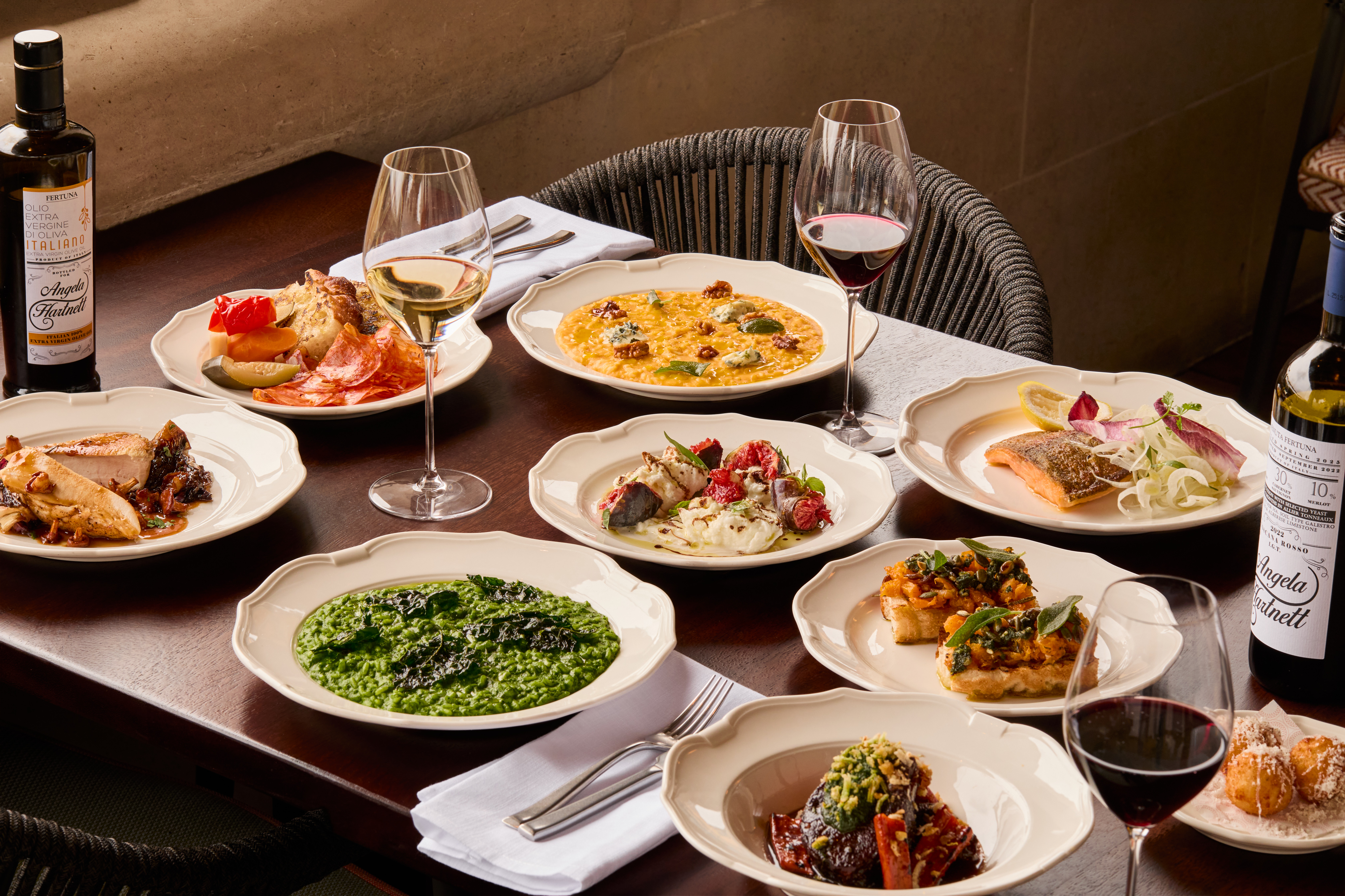 Plates of artfully styled food and glasses of red and white wine are arranged on a round marble table. The display contains menu items from Cicoria, Angela Hartnett's restaurant at the Royal Opera House.