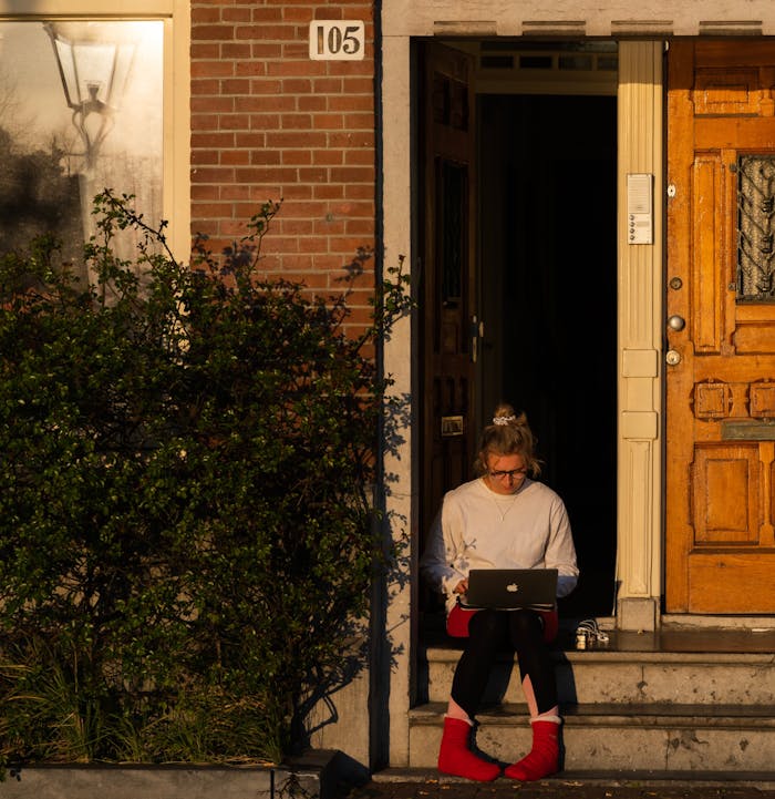 Een meisje op haar laptop in de deuropening van haar huis