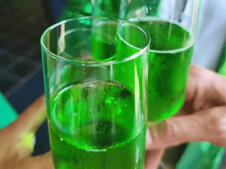 Twee handen proosten met een glas gevuld met groene champagne