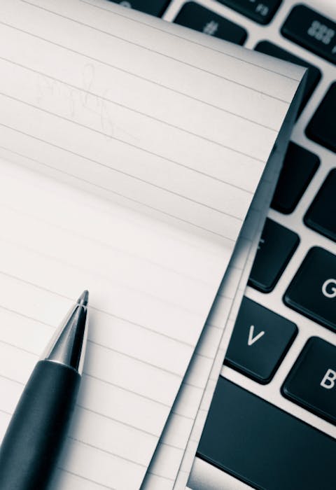 Een notitieblok en een pen liggend op een toetsenbord