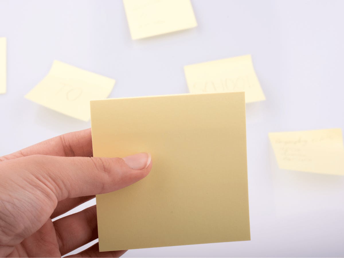 Five empty post-its on a white wall with in front of it a hand holding a pack of post-its