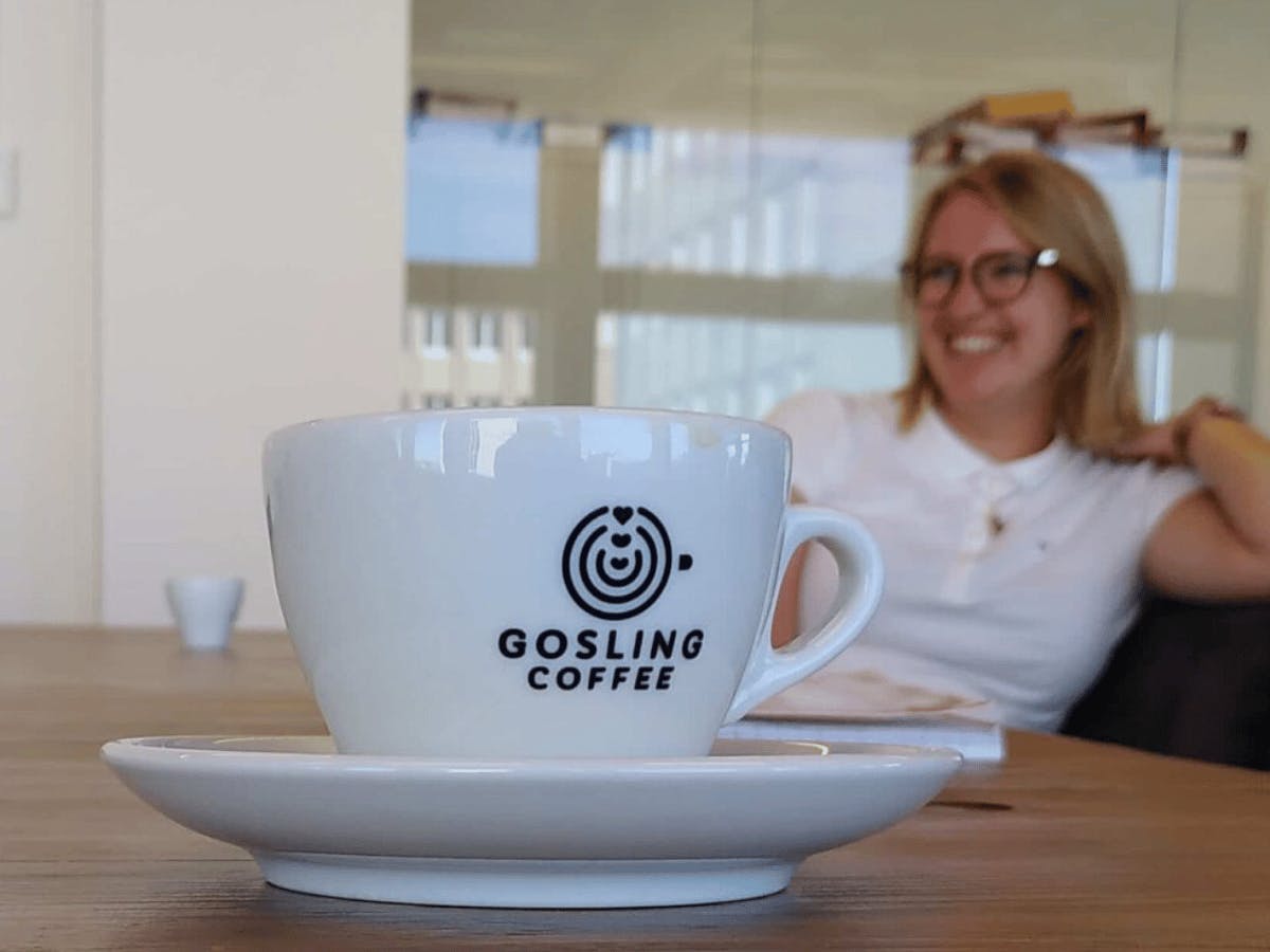 Ingezoomde foto van een witte kop en schotel op tafel met het logo van Gosling koffie erop
