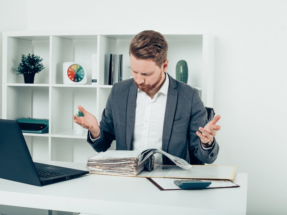 Een persoon die aan een bureau zit met een laptop en papieren