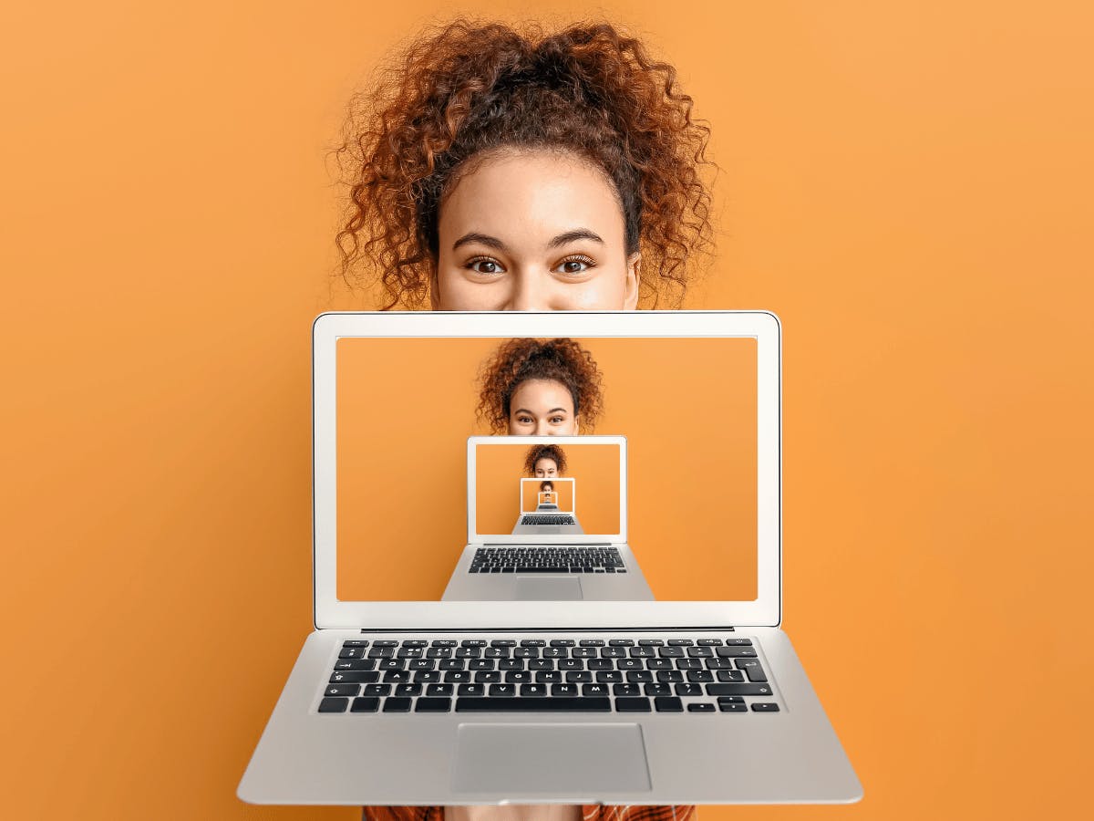 Een persoon met krullend haar die een laptopscherm omhoog houdt
