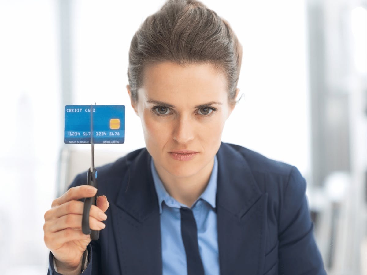 Een persoon in een pak die een creditcard tussen een schaar omhoog houdt