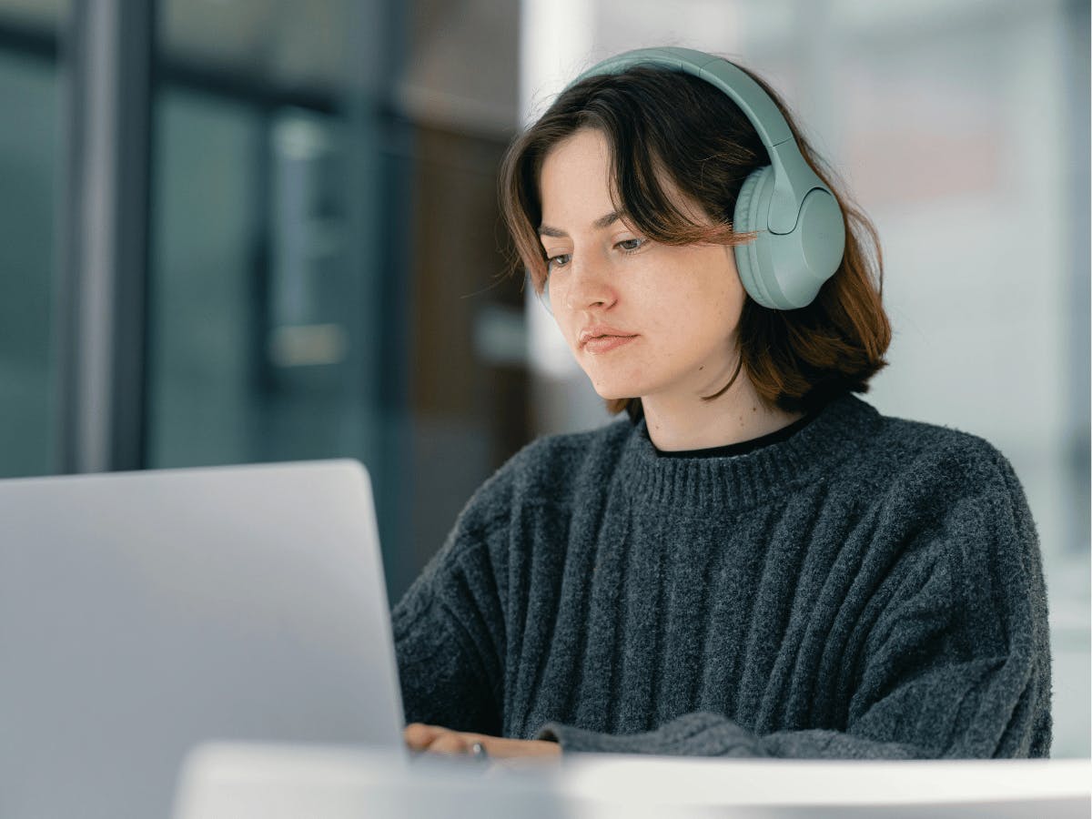 Een persoon die een koptelefoon draagt terwijl ze op een laptop werkt.