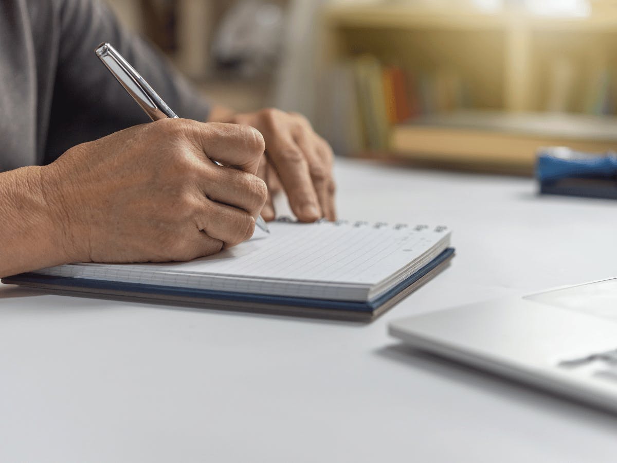 Een persoon zit aan een bureau en schrijft in een notitieboekje