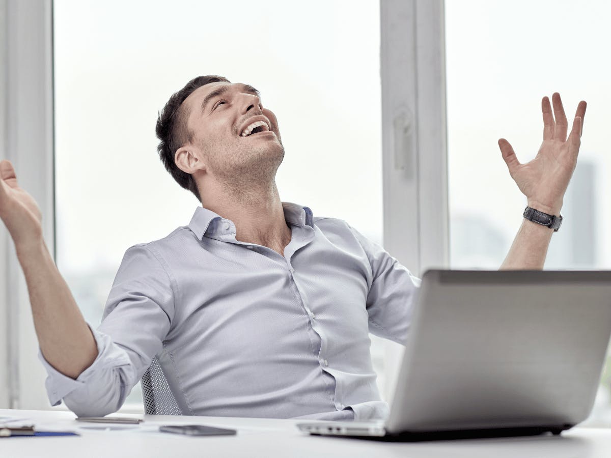 Een persoon die glimlacht terwijl hij aan een bureau zit met zijn handen in de lucht