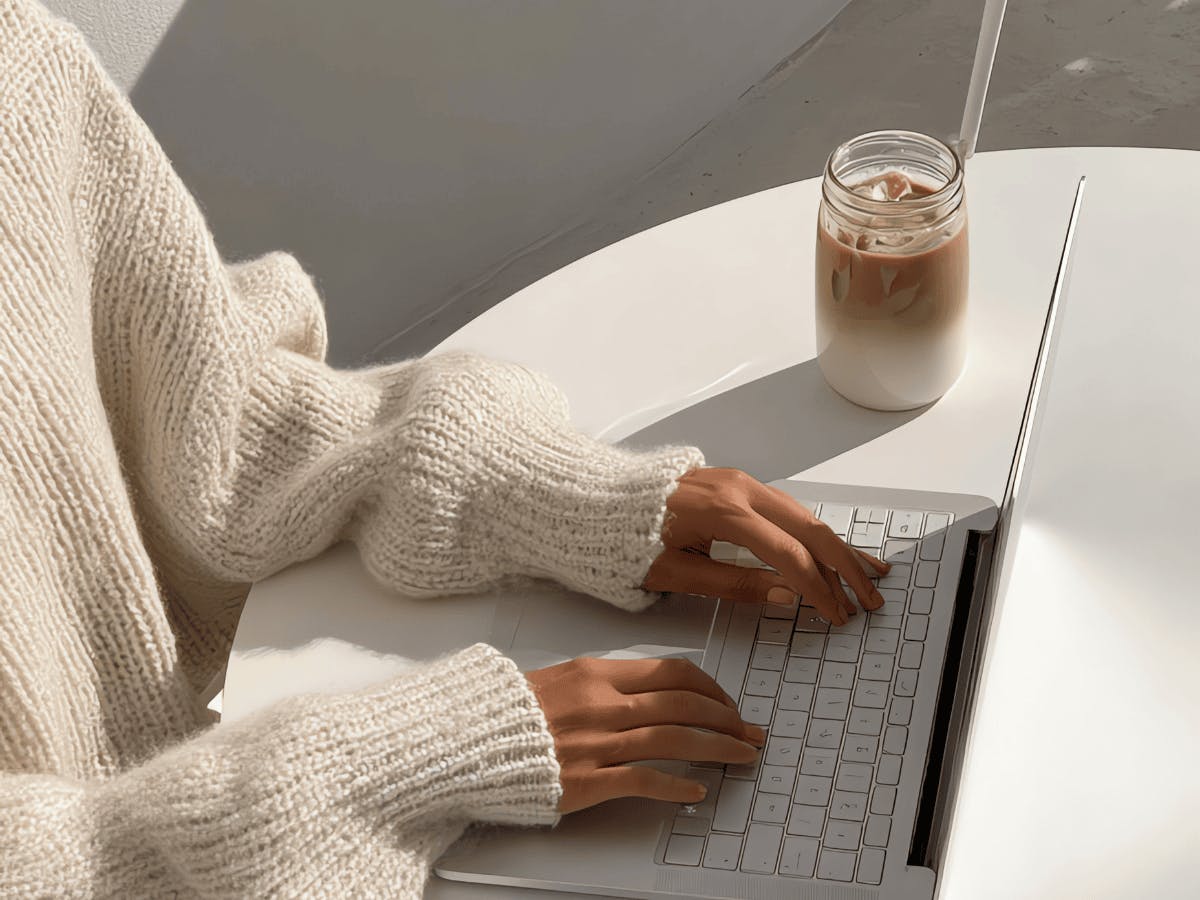 Een persoon die aan een witte tafel zit met een laptop
