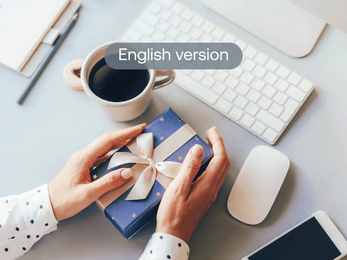 Hands with blue Christmas gift on desk with coffee and keyboard – corporate Christmas gifts and work-related costs scheme