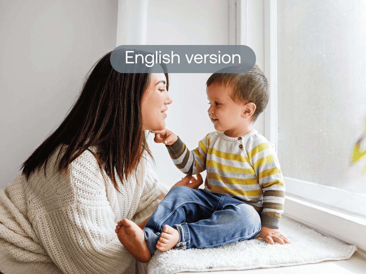 A person in a white sweater sits next to a window with a young child in a striped shirt and jeans.