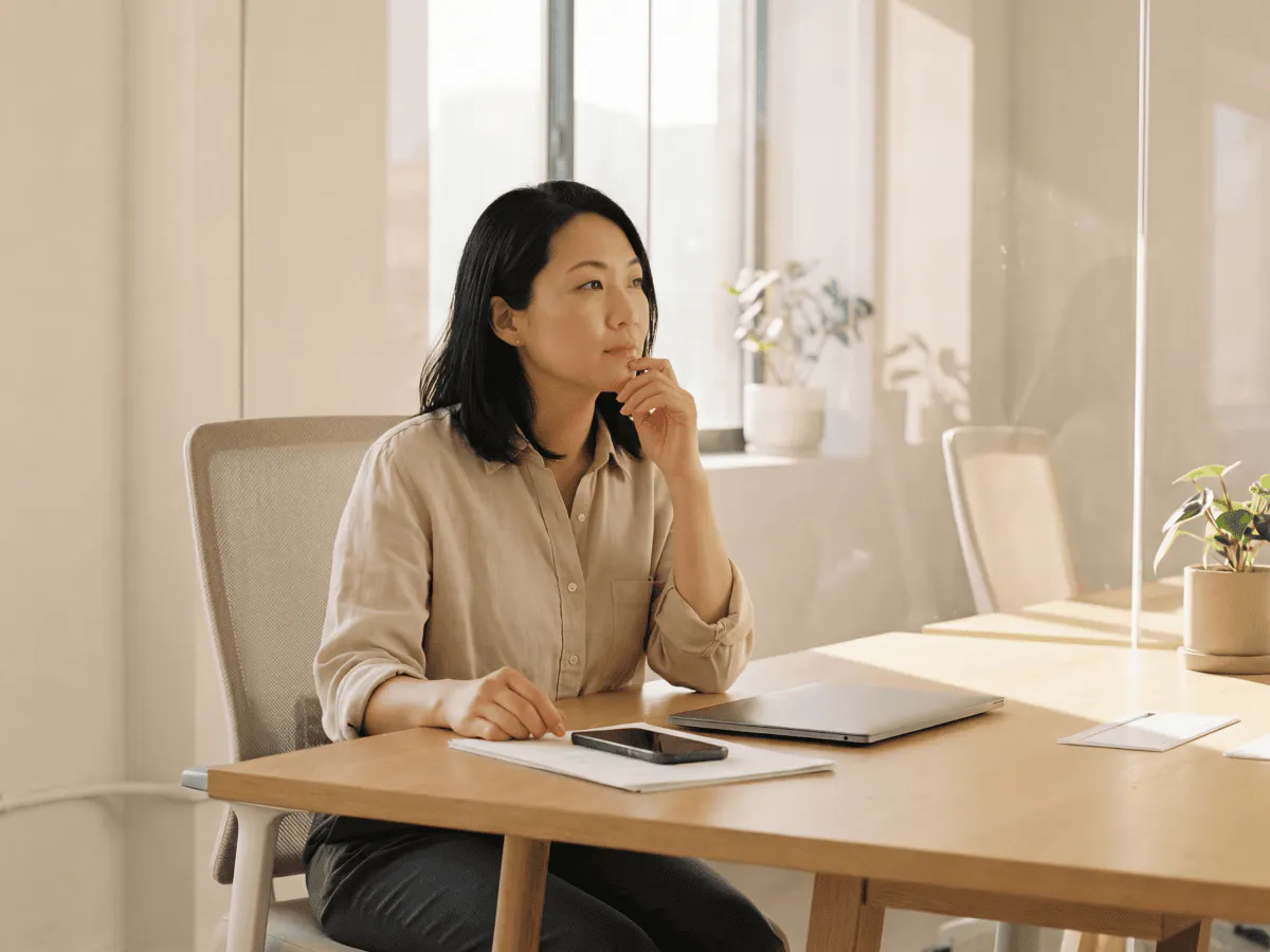 Iemand zit aan een bureau in een kantoor met een dichtgeklapte laptop voor zich. Hij of zij kijkt opzij met de hand tegen de kin.
