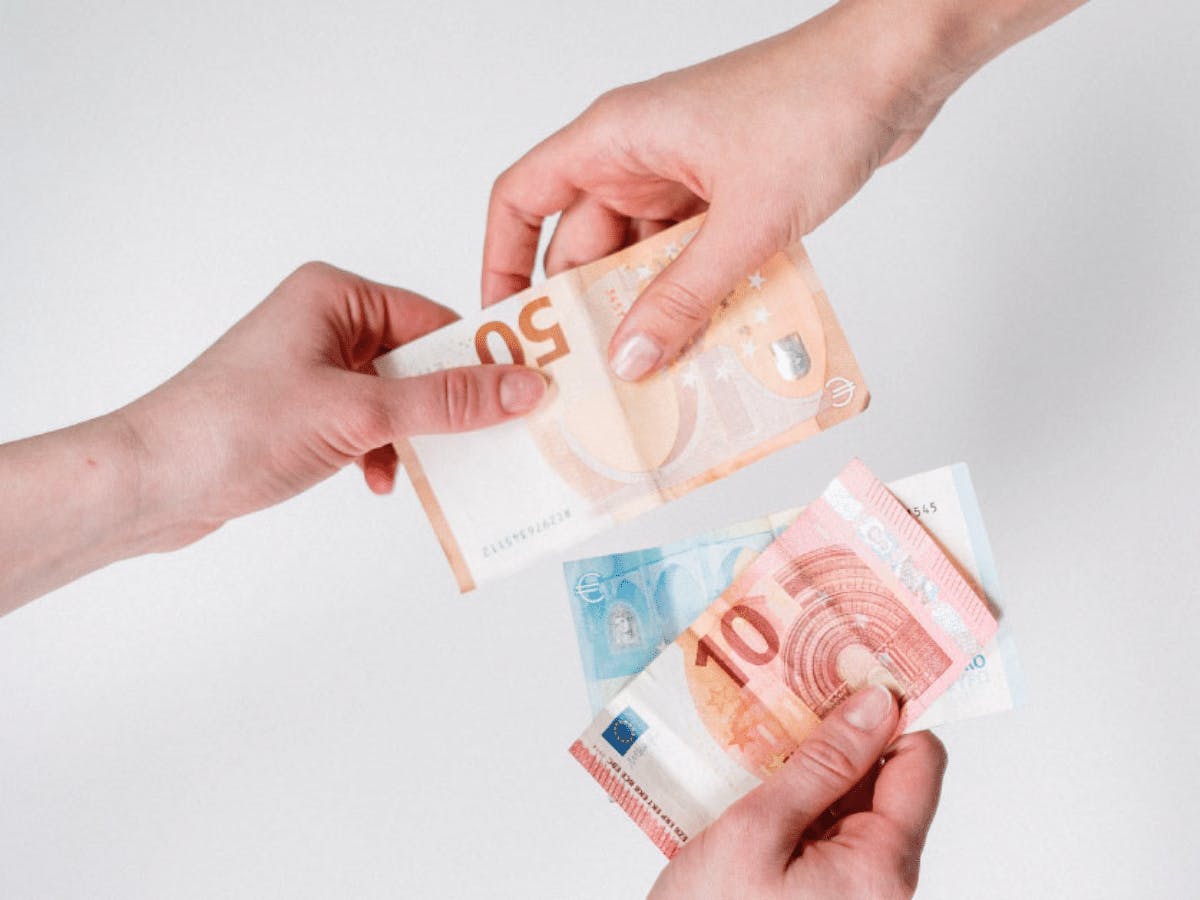 Twee handen die een biljet van 50 euro uitwisselen en in de andere hand zit een biljet van 10 en 20 euro.