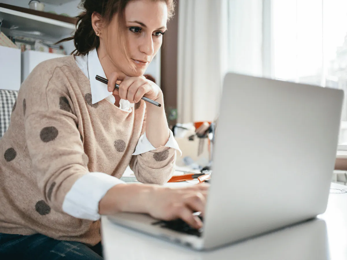 Iemand die achter een bureau zit met een laptop met een pen in de hand.