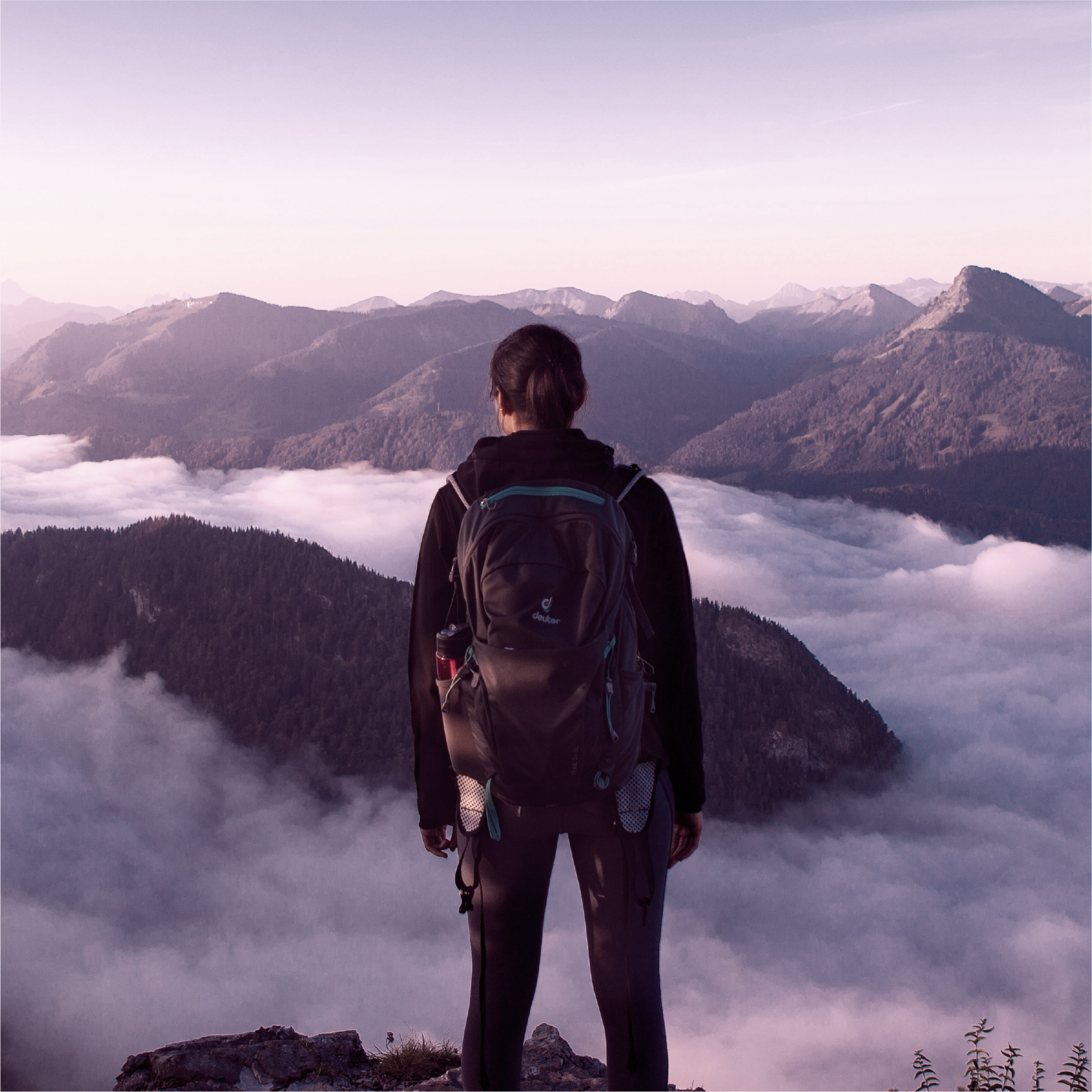 Hiker with backpack overlooking a mountain range with clouds.