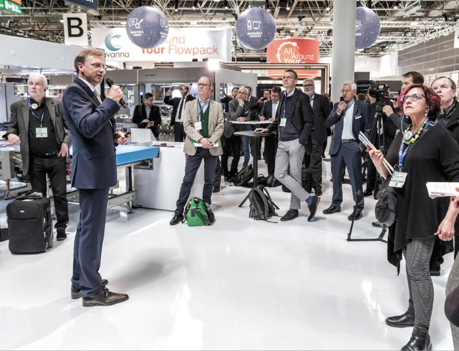 Ein Sprecher hält auf einer Messe einen Vortrag zum Thema hybride events, viele Menschen lauschen gespannt dem Redner