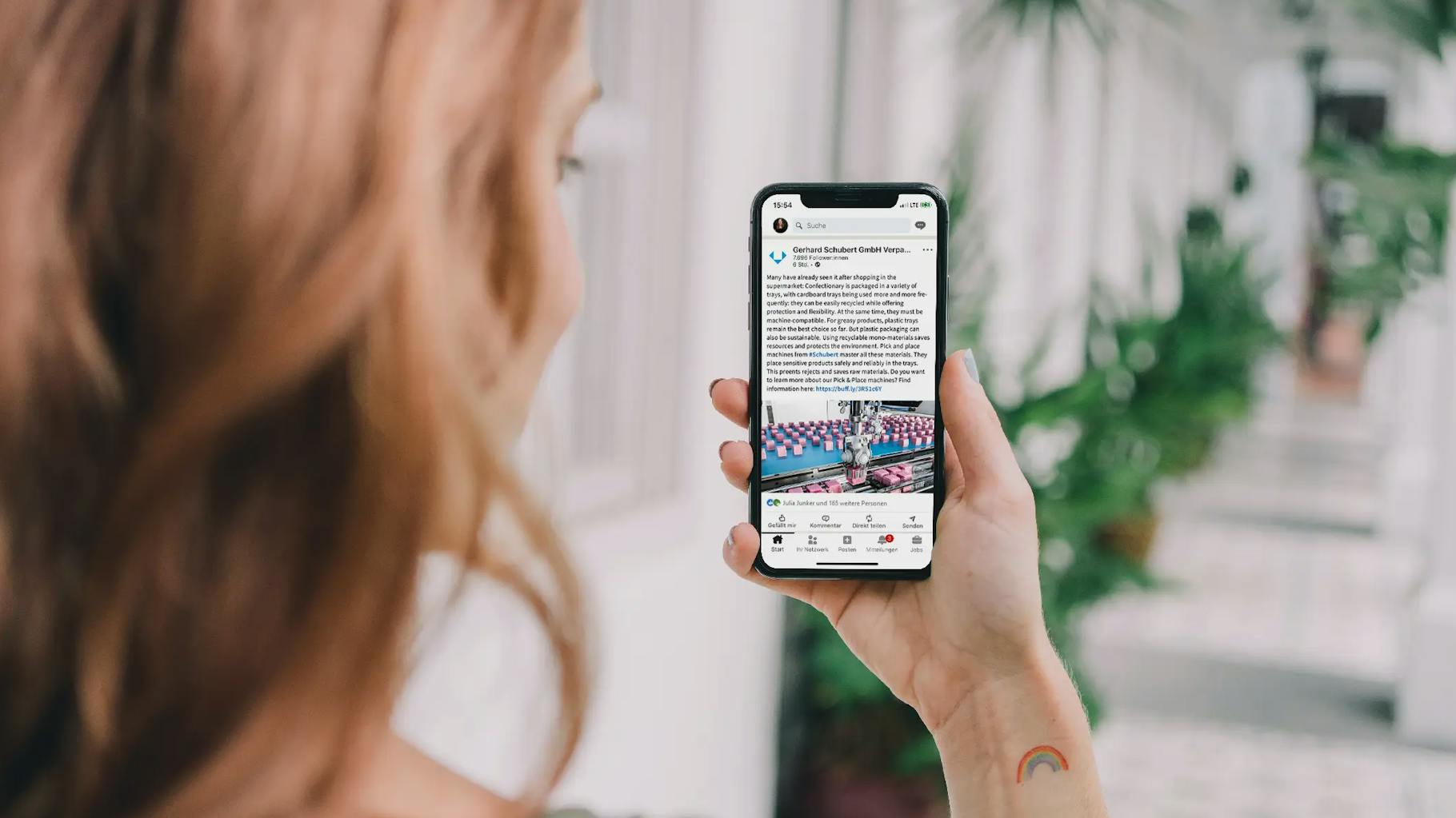 Blick über die Schulter einer blonden, langhaarigen Frau, die auf ihrem Handy einen LinkedIn Post der Firma Schubert anschaut