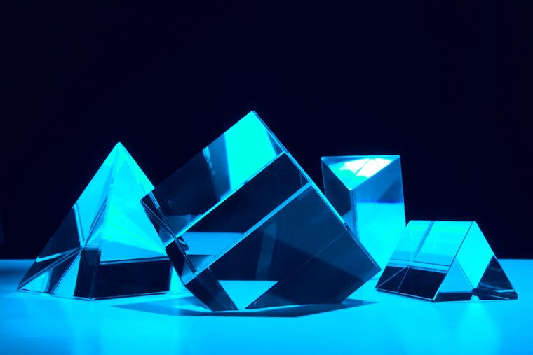 Abstract art of a cube, a pyramid and two triangles to form software system architecture with light refractions and reflections on the surface.