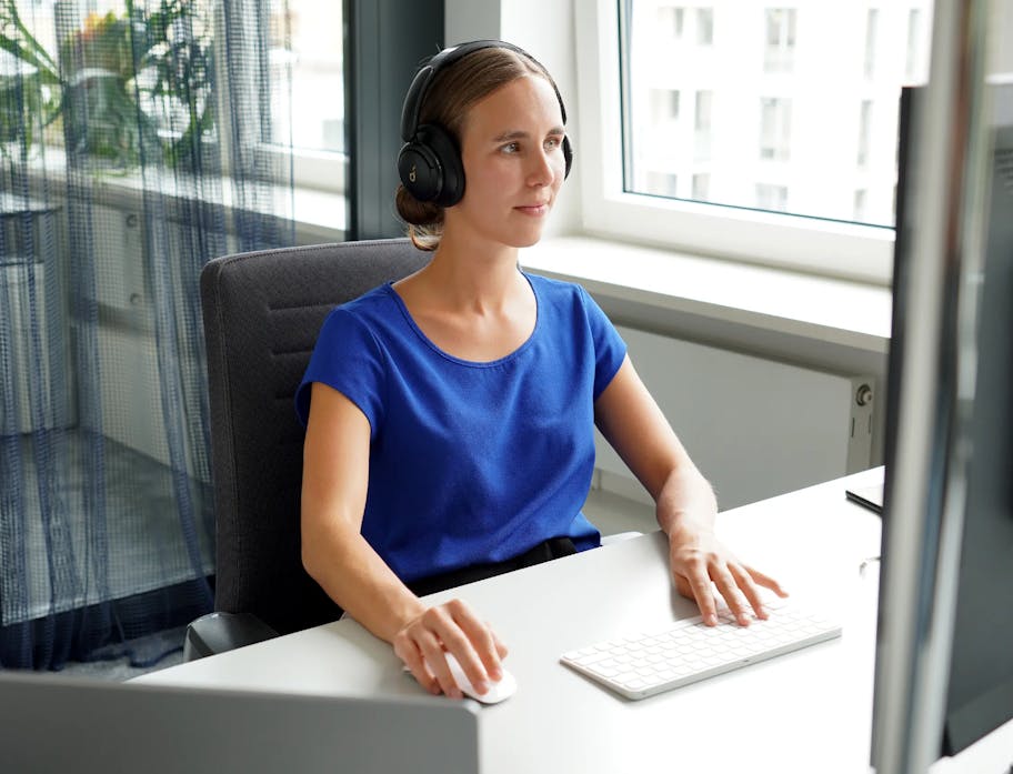 A young woman sitting at a PC with headphones on and working