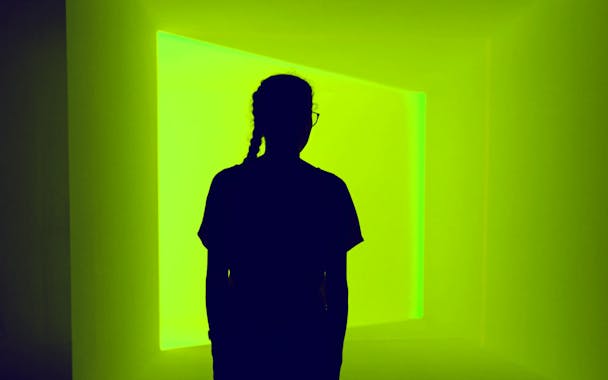 Ästhetische Nahaufnahme einer Person, in dunkel gehüllt, die vor einem hellen, dreidimensional wirkenden Lichtfenster steht