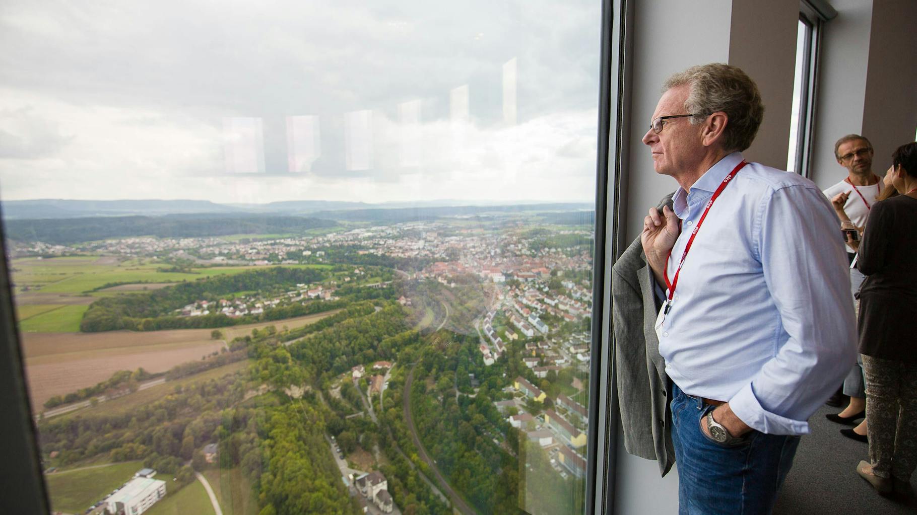 Ein grauhaariger Mann mit Hemd gekleidet, der die Landschaft aus dem 232 Meter hoch gelegenen Fenster des Thyssenkrupp Testtowers in Rottweil betrachtet