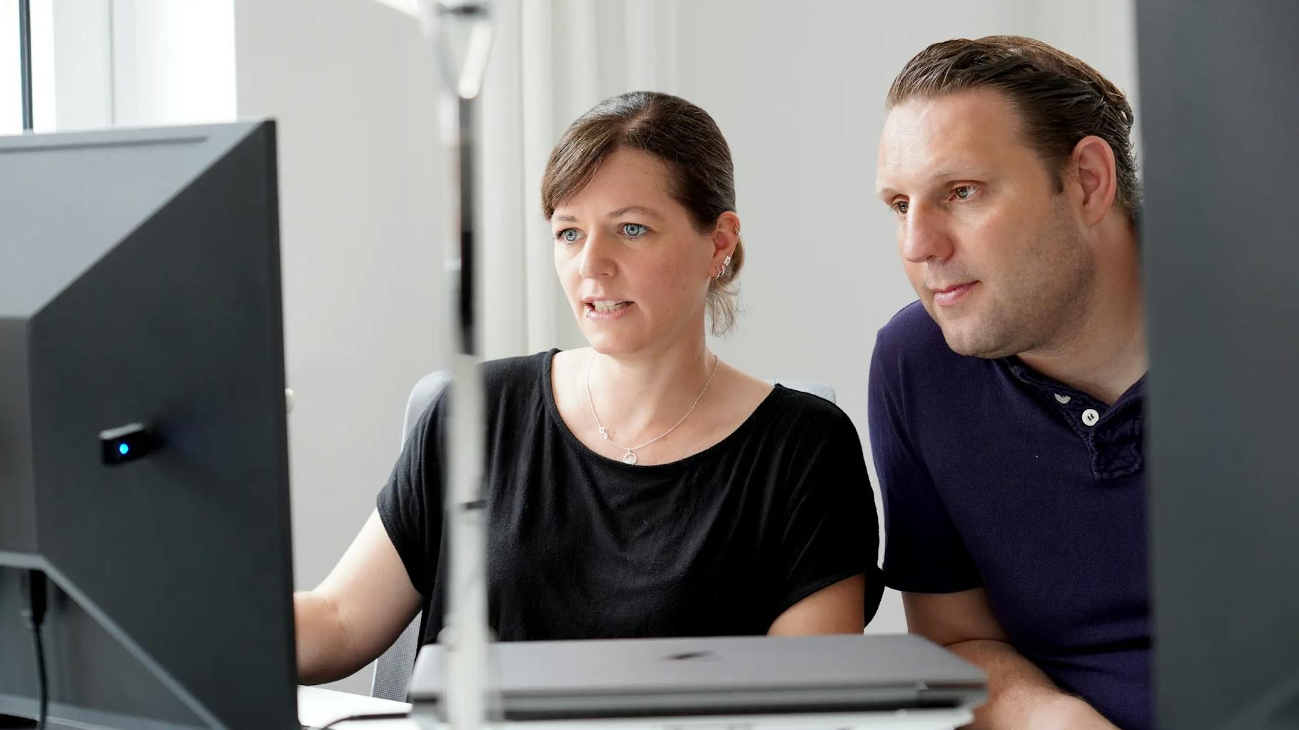 Zwei Mitarbeiter der Ruess Group Standort München unterhalten sich über etwas, dass auf einem Monitor abgebildet ist.