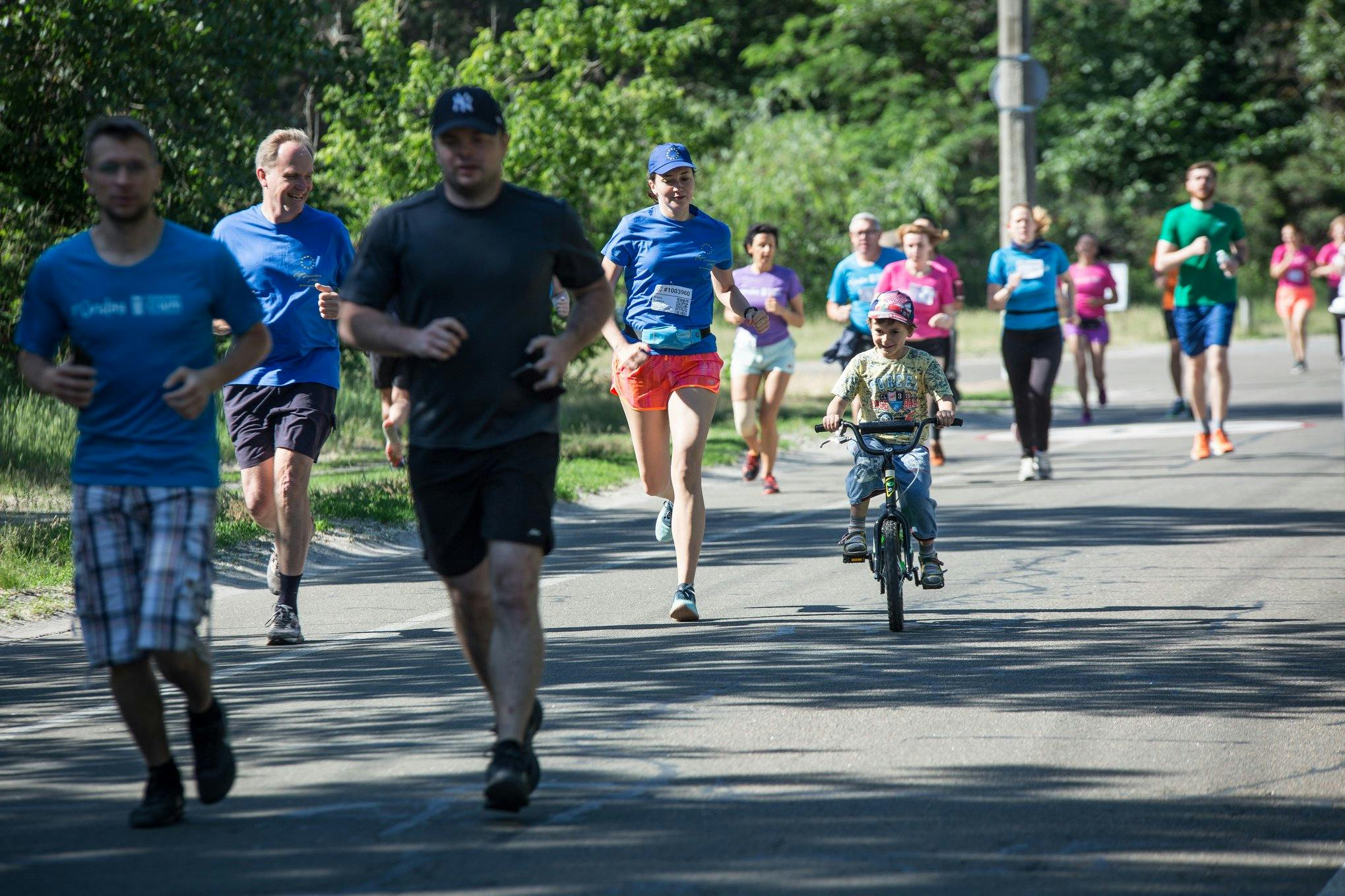 In the picture: participants of the Runday race during a 5 km run, adults are running, a boy is riding a bicycle next to his mother