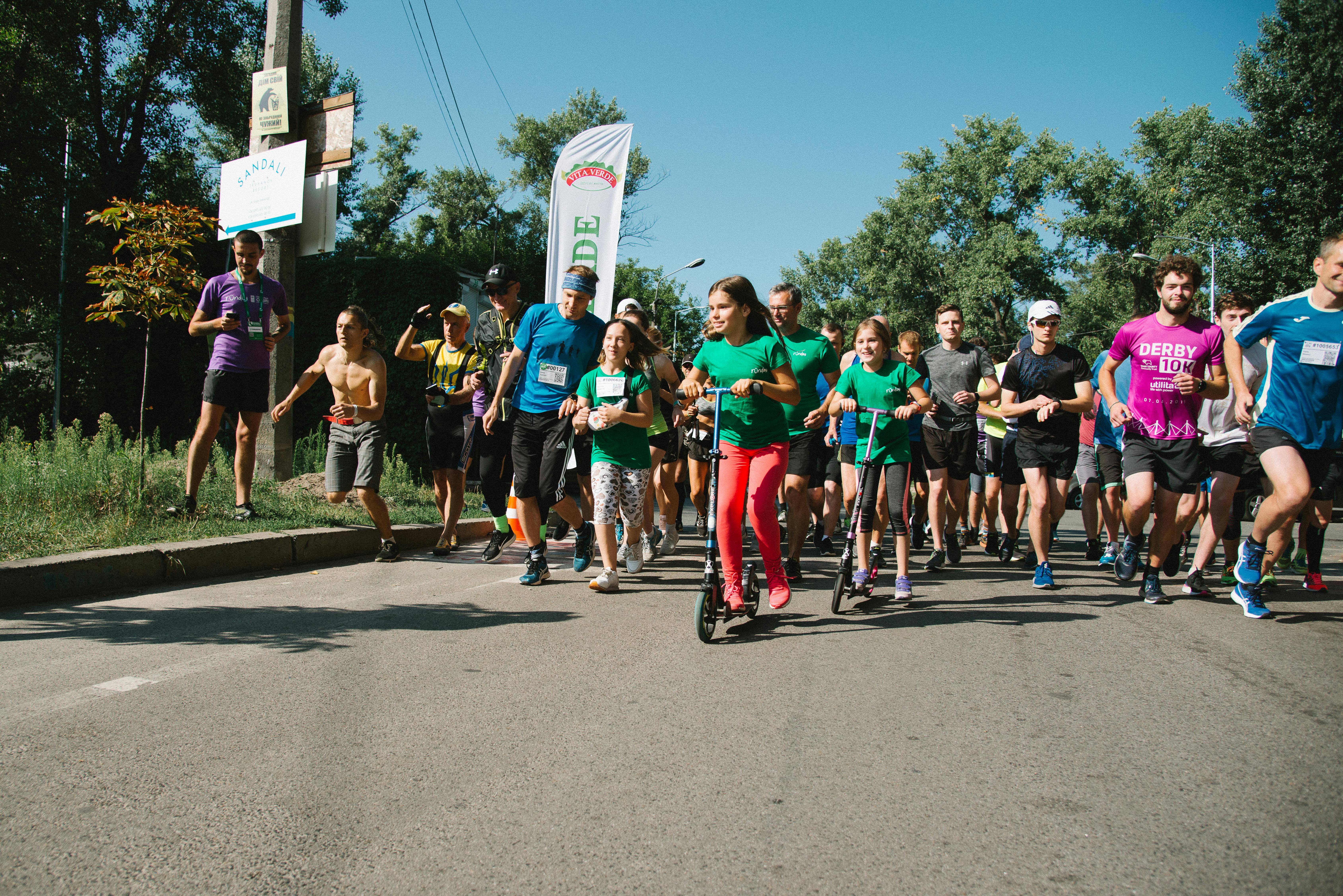 The picture shows the start of the weekly 5 km Runday race, participants are starting, in the foreground are teenage girls on scooters