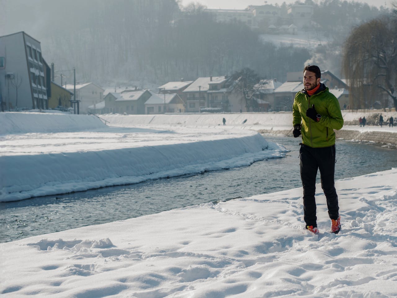 На зображенні - чоловік біжить по снігу біля річки