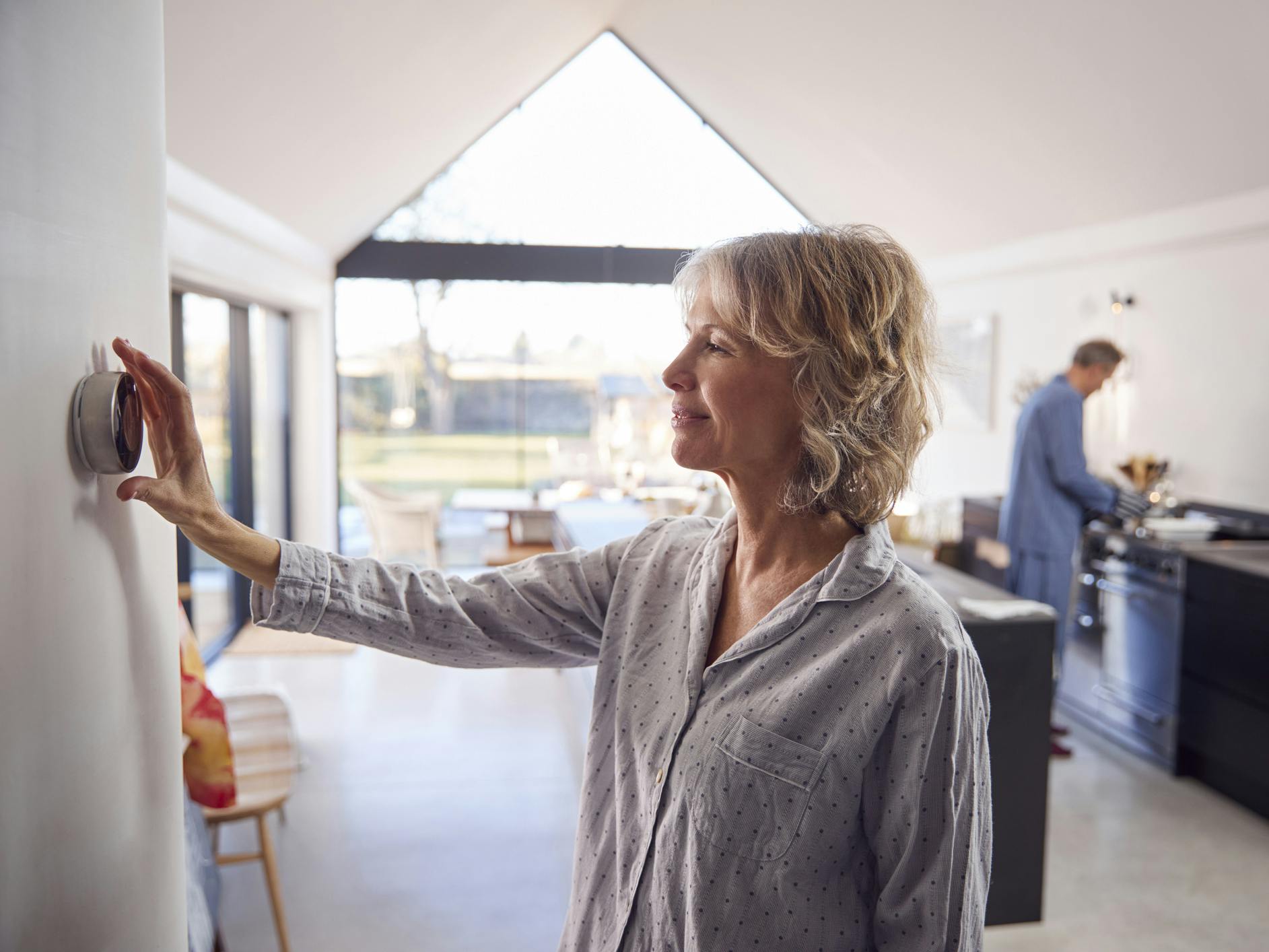 Mature Woman Adjusting Wall Mounted Digital Central Heating Thermostat Control At Home