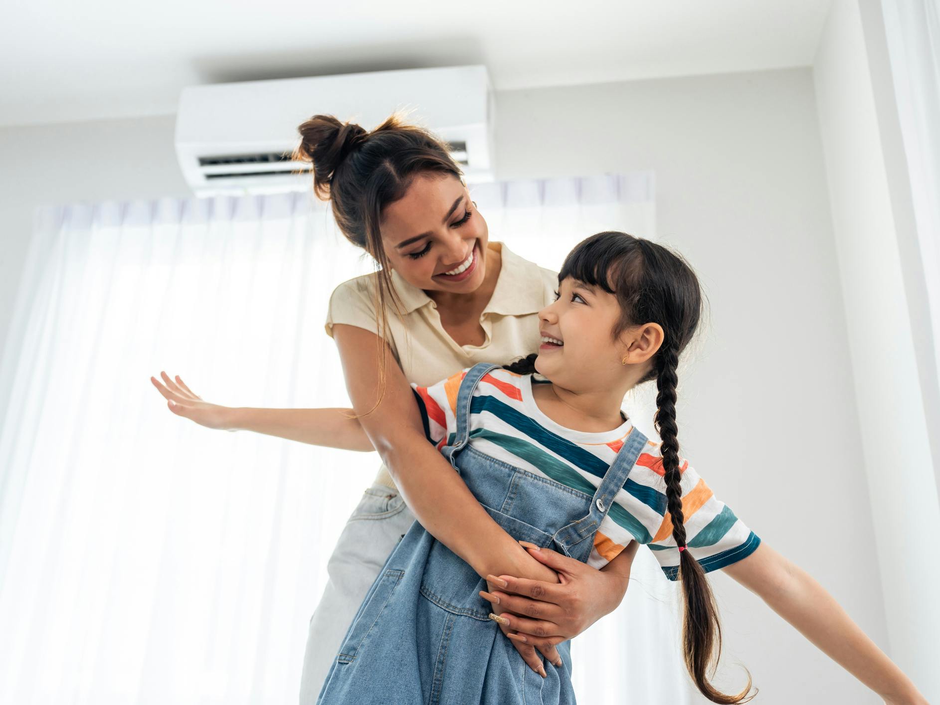 Adorable young girl daughter hug mother while playing with happiness in living room