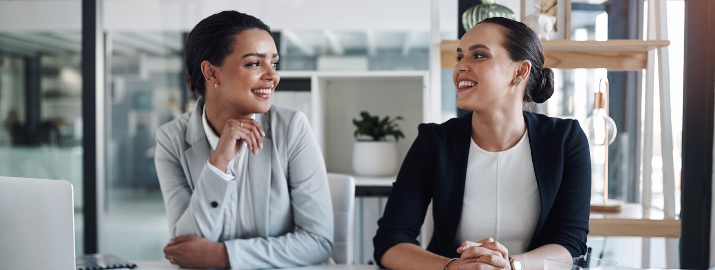 Two women are smiling at each other, knowing that the cybersecurity services by s01ve Ltd. are protecting their business.