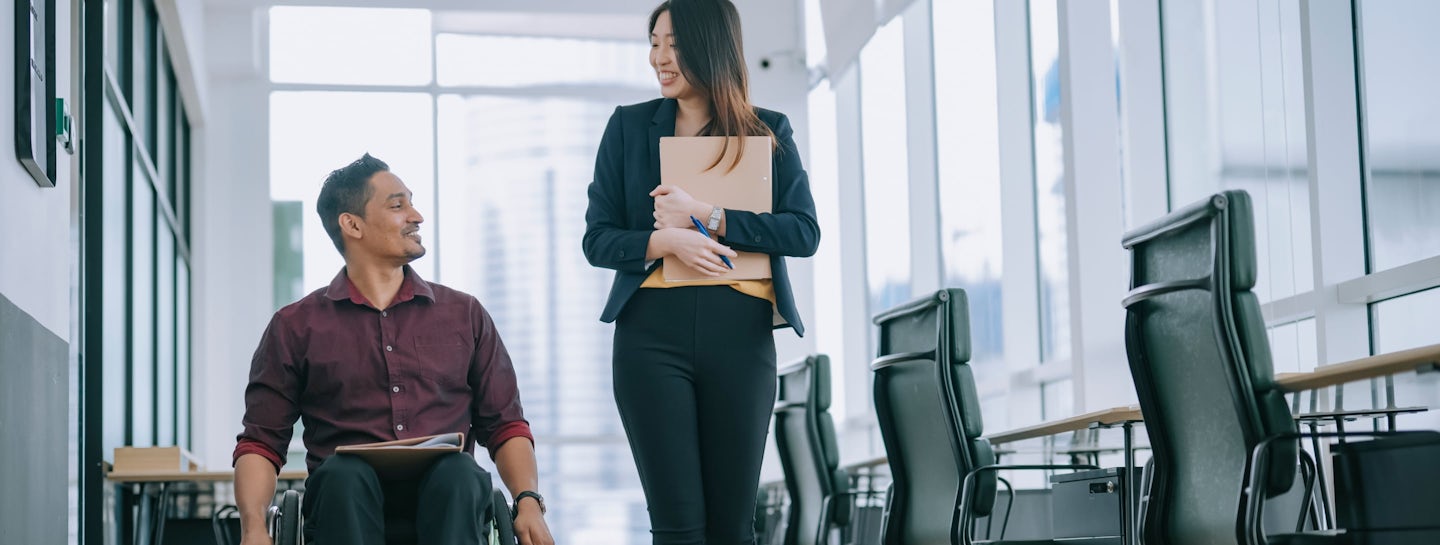 A man in a wheelchair and a woman walking beside him while discussing something. They look happy and content representing s01ve Ltd. as a safe and inclusive workplace.