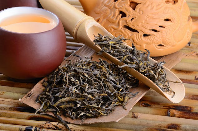 oolong tea leaves on a spoon with cup of tea next to it 