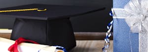 graduation cap and diploma next to graduation gift in a wrapped box