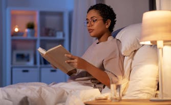 person reading from bed with bedside reading lamp next to them