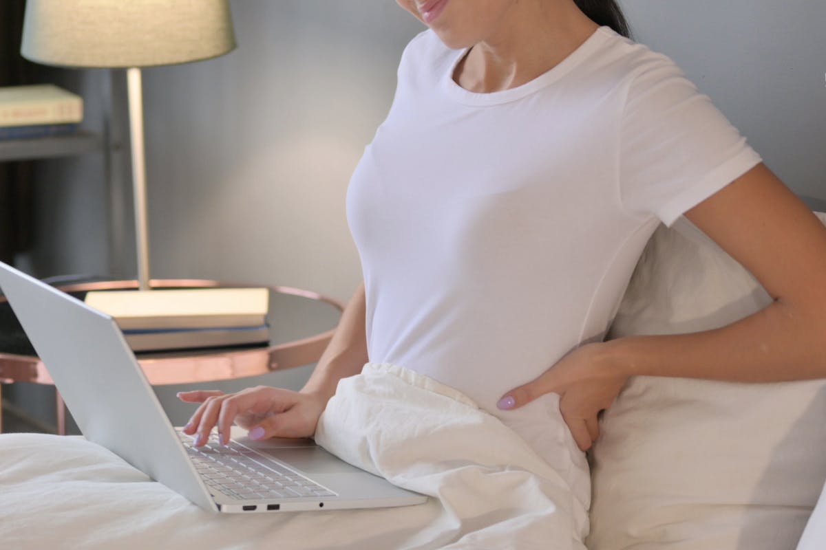 person with back pain using computer in bed