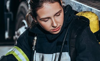 tired firefighter sitting against firetruck