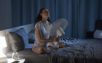 person using a fan in bed to cool down before sleep