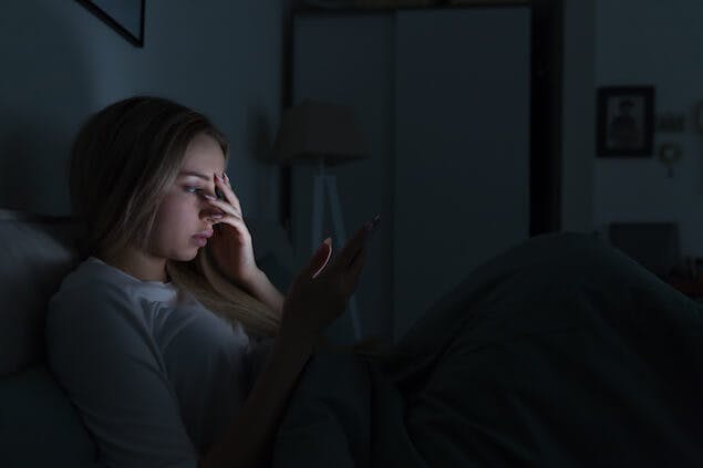 image of stressed person looking at election results on phone in bed