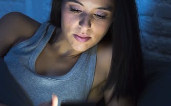 person looking at phone, which emits blue light, in bed