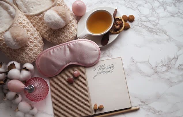 journal to write night affirmations in, sleep mask, slippers, and cup of tea