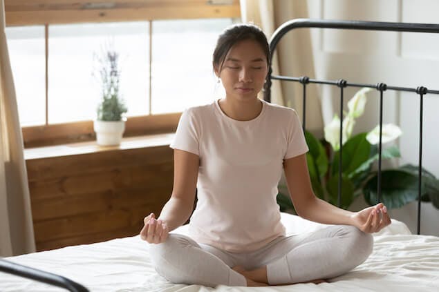 image of person meditating on bed to relieve headache-causing stress
