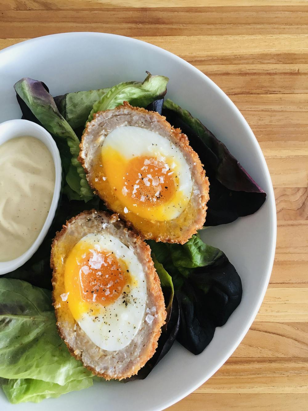 scotch eggs on a plate with salad and mustard sauce