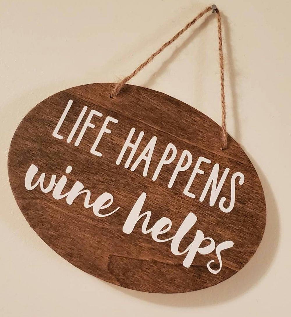 wooden sign with the words "life happens wine helps" on it