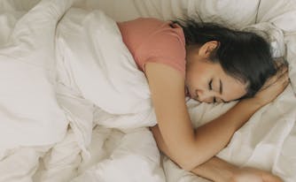 person sleeping on stomach in bed with arm under head
