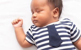 baby sleeping on top of bed with arm raised