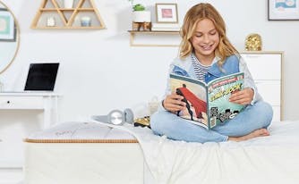 child sitting on full-size bed reading comic book