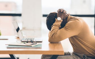 person with burnout with head in hands falling asleep at desk